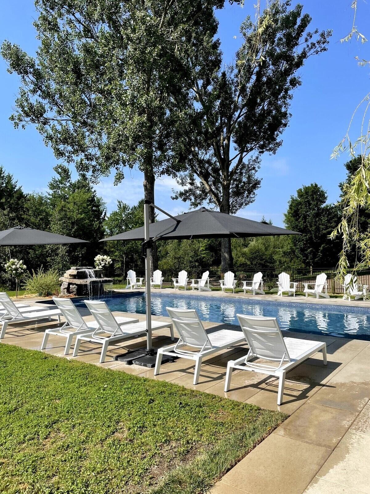 A poolside area with lounge chairs and umbrellas, surrounded by trees and a small waterfall feature.