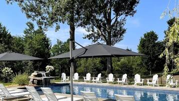 A poolside area with lounge chairs and umbrellas, surrounded by trees and a small waterfall feature.