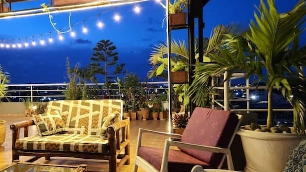 Terraza en la azotea con muebles de madera, plantas en macetas y luces colgantes.