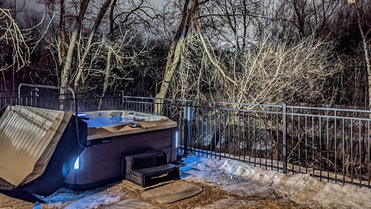 Una vasca idromassaggio con coperchio, circondata da una recinzione metallica, con sullo sfondo alberi spogli.