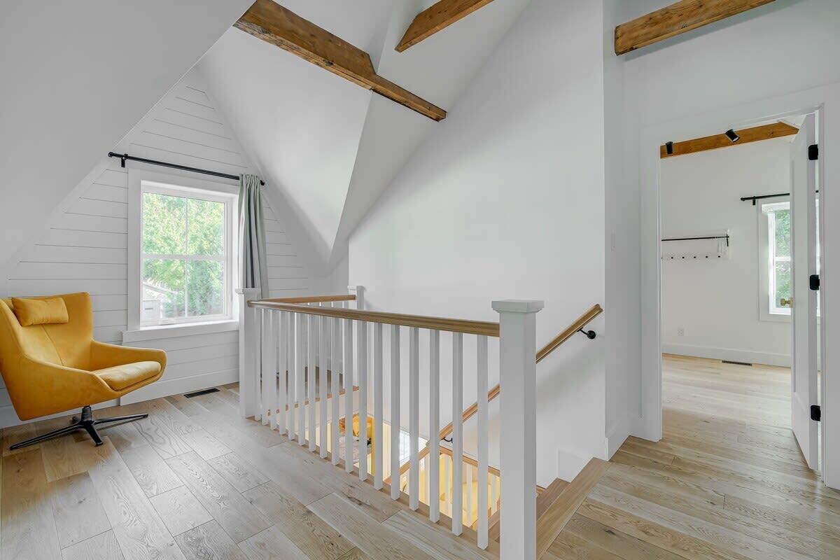 Ein geräumiges Schlafzimmer im Loft-Stil mit hohen Decken, freiliegenden Holzbalken, einer Holztreppe und einem großen Fenster.