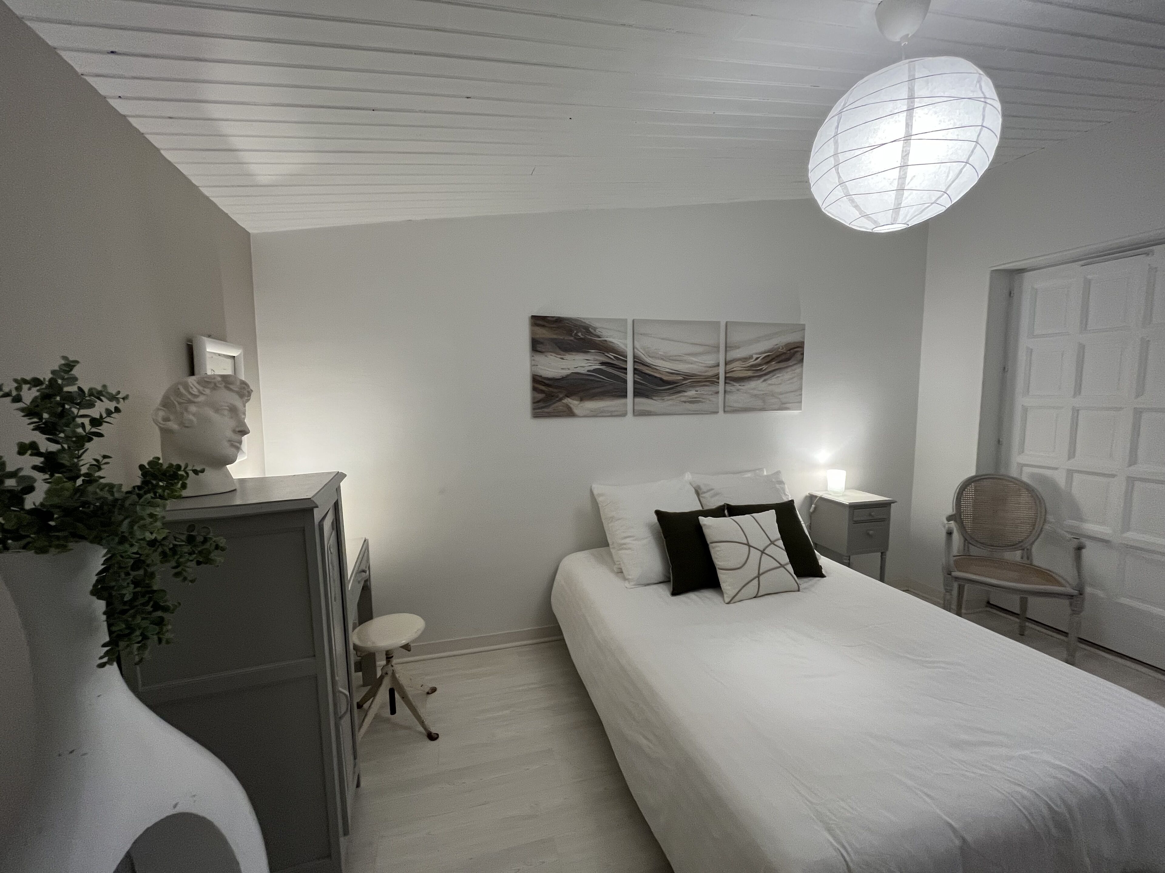 Een slaapkamer met een bed, een bureau, een stoel, een borstbeeld en abstracte decoratie aan de muur.