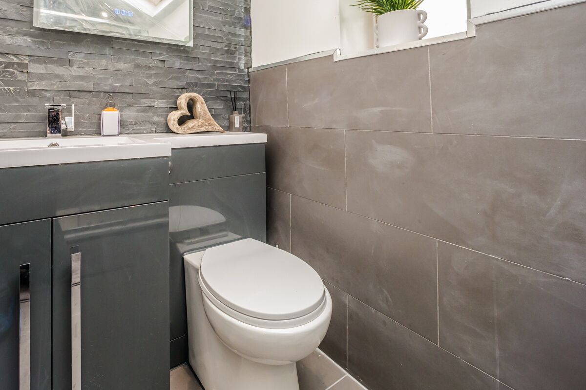 A modern bathroom with a white toilet, dark grey cabinets, and a grey tiled wall.