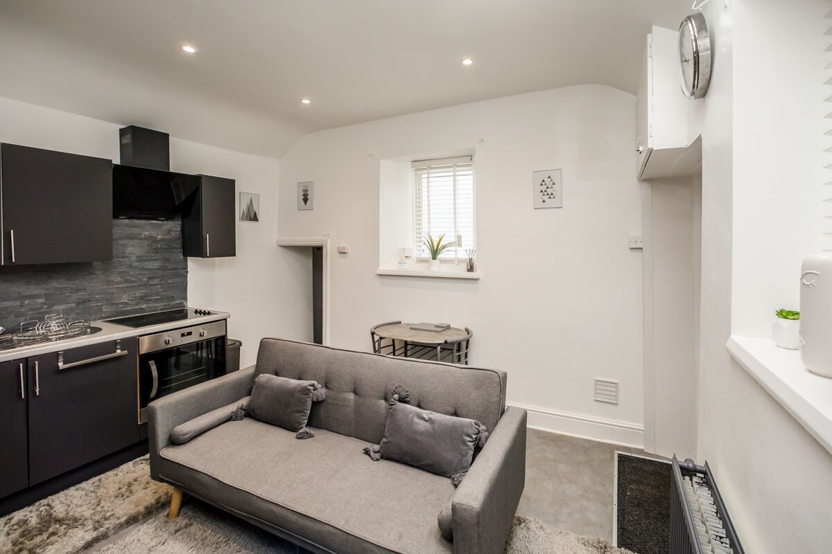A modern kitchen with dark cabinets, a gray sofa, and a small dining table.