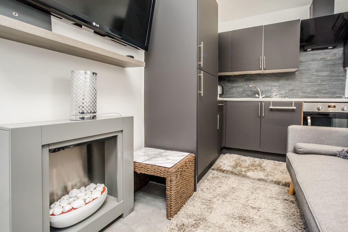 A modern kitchen with grey cabinets, a built-in oven, and a flat-screen TV mounted above the counter.