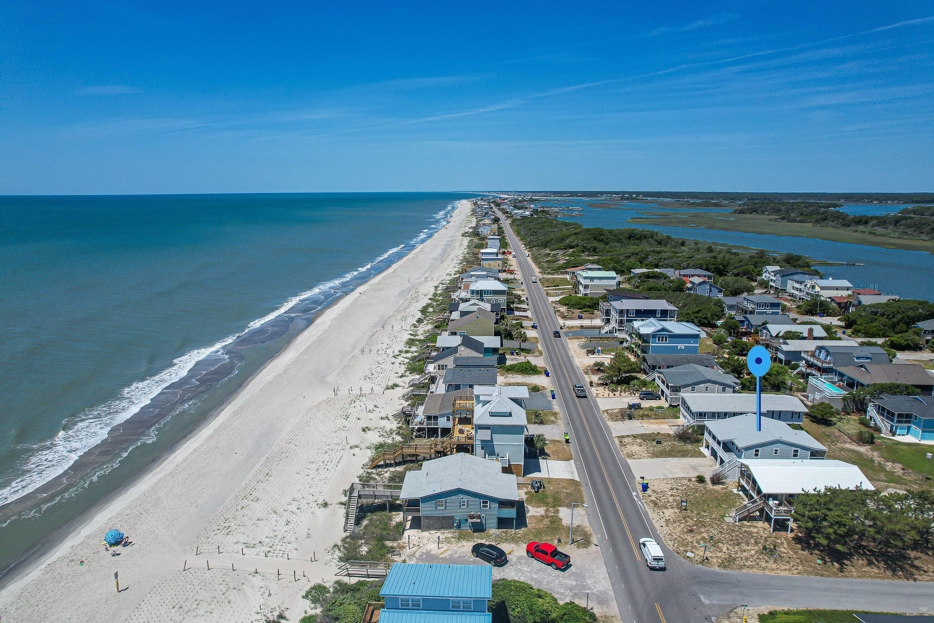 A coastal residential area with houses along the beach, a road, and a clear view of the ocean.
