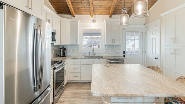 A modern kitchen with stainless steel appliances, white cabinetry, and a wooden ceiling.