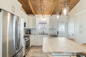 Una cucina moderna con elettrodomestici in acciaio inox, mobili bianchi e soffitto in legno.