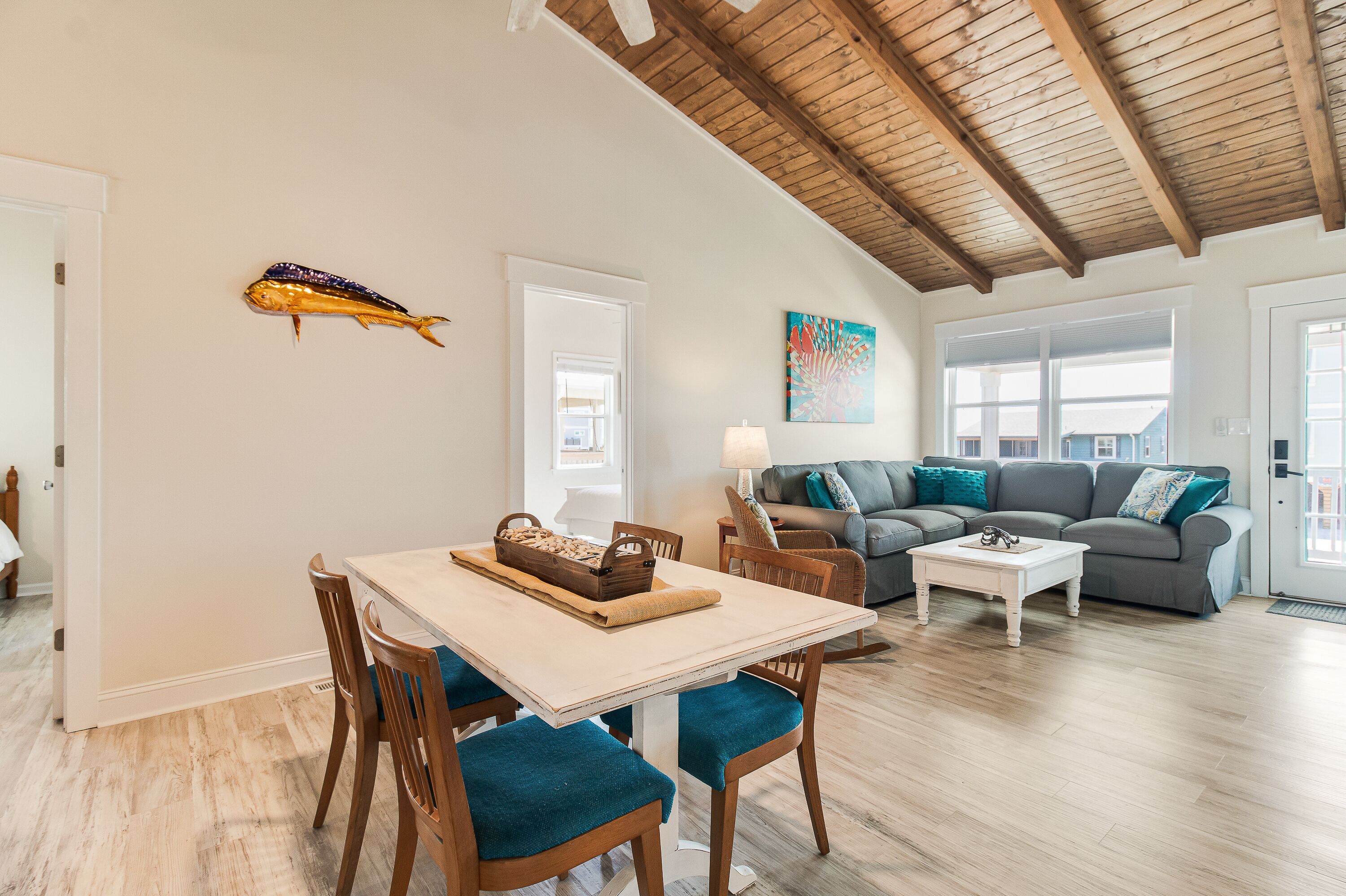 Een ruime woonkamer met houten plafond, een eettafel met stoelen, een bank en een salontafel.