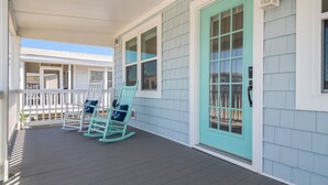 A covered porch with rocking chairs and a teal door.
