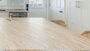 A kitchen with white cabinets, a marble countertop, and pendant lights.