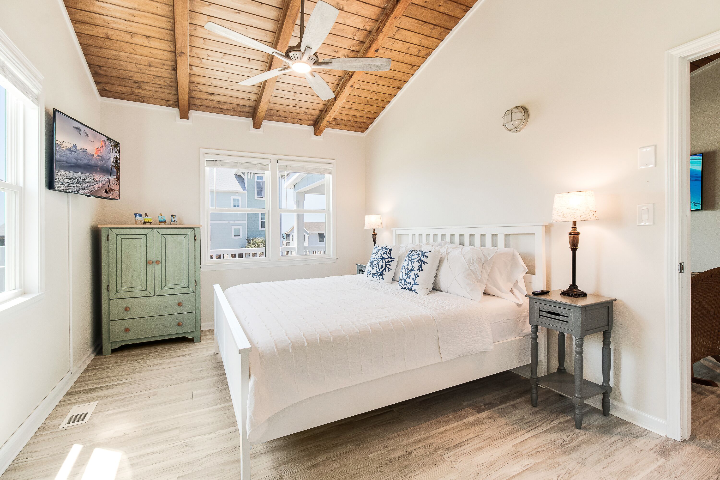 A bedroom with a wooden ceiling, a bed with white bedding, a green cabinet, and a nightstand with a lamp.