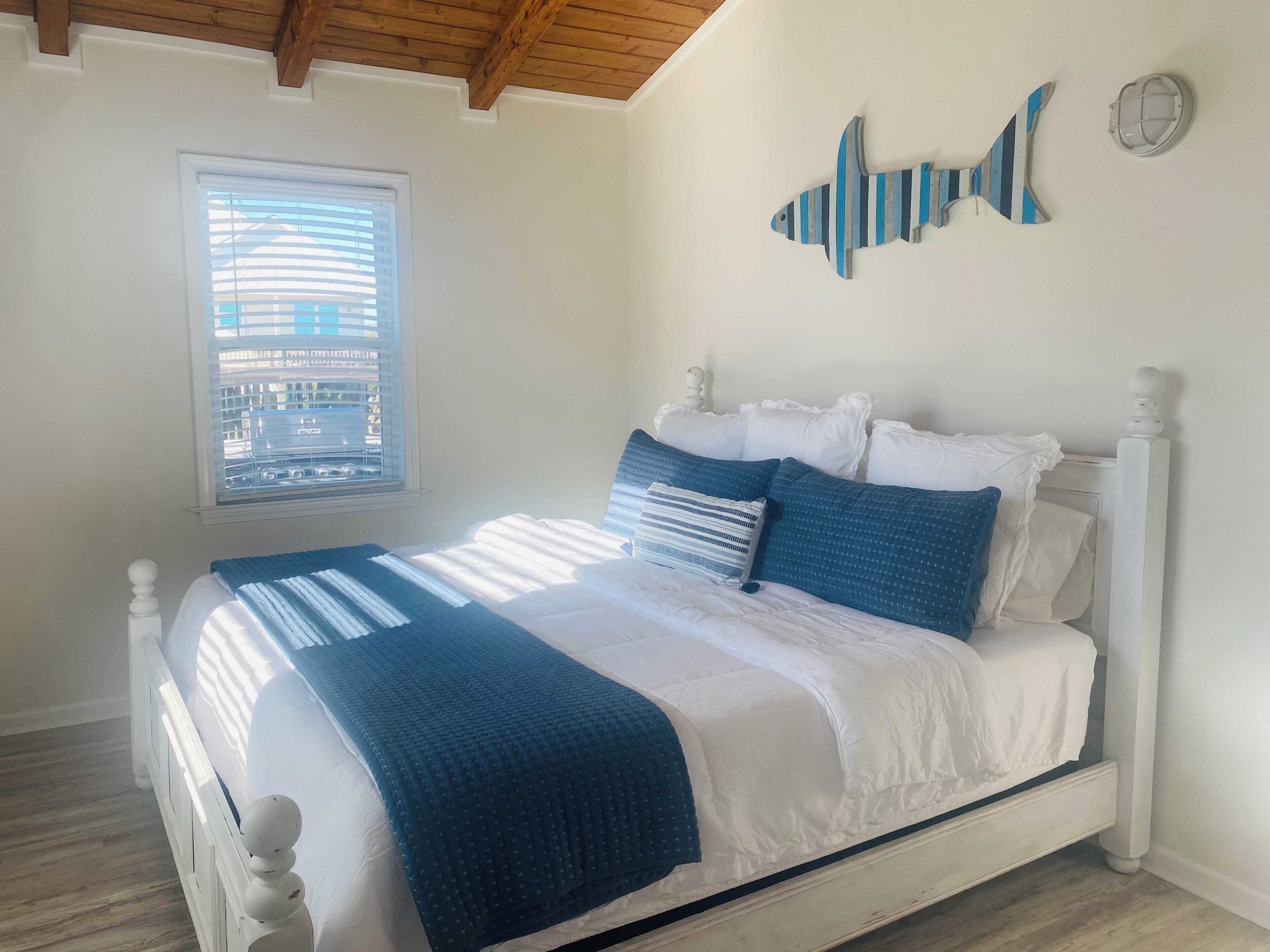 A bedroom with a bed, white bedding, a window, and a wall decoration.