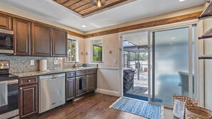 A kitchen with wooden cabinets, granite countertops, stainless steel appliances, and a sliding glass door leading to an outdoor patio.