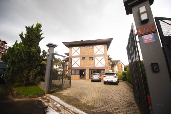 A building with a brick facade, a gated entrance, and two cars parked in front. - Loft Lindo com Ar Condic, WIFI, Perto de Capivari (Campos do Jordão)