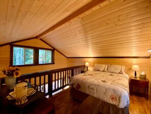 Cozy single-room accommodation with a sloped ceiling, featuring a bed, bedside tables, and a window with an outdoor view.