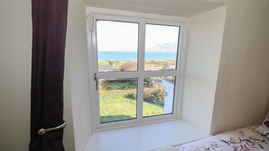 Een kamer met een raam dat uitkijkt over een kustlandschap.