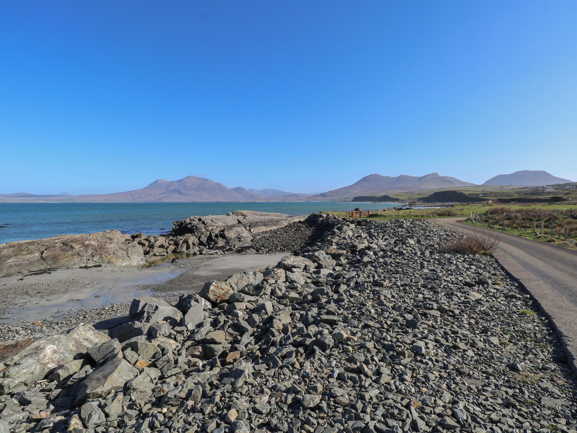 A rocky coastal road with a clear view of the sea and distant mountains.