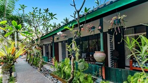 A pathway lined with tropical plants and a building with a tiled roof and large windows. - Nawasakti Resort (Ubud)