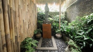 A narrow garden with a stone statue, bamboo fence, and potted plants. - Nawasakti Resort (Ubud)