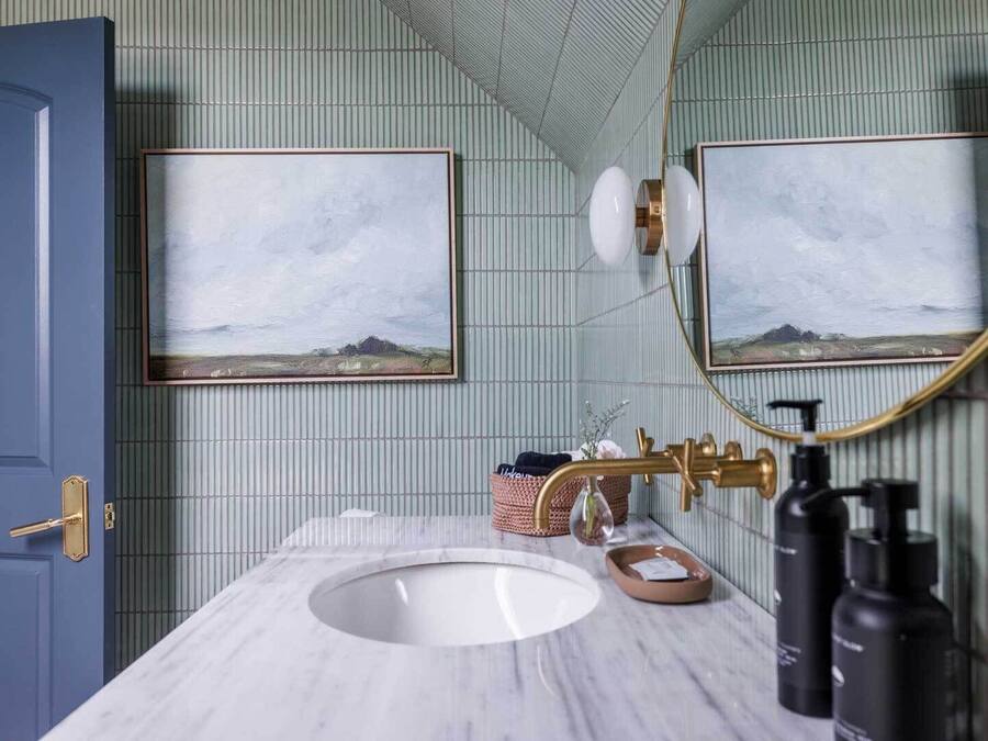 A bathroom with a marble sink, gold fixtures, and two framed landscape paintings on the wall.