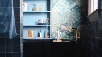 A bathroom with a blue tiled wall, a sink with a gold faucet, and a shelf with toiletries.