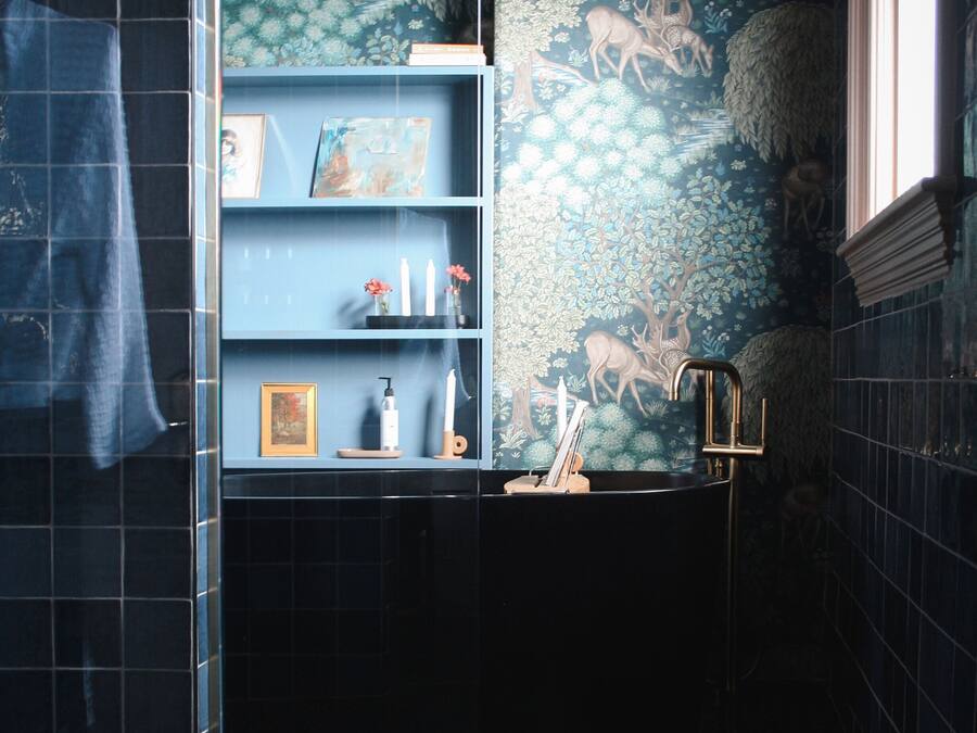 A bathroom with a blue tiled wall, a sink with a gold faucet, and a shelf with toiletries.