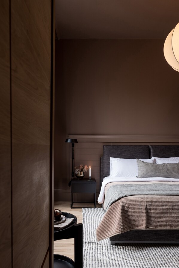 Ein modernes Schlafzimmer mit einem dunklen Holz-Kopfteil, einem Nachttisch mit Lampe und einem Bett mit gestreiftem Überwurf.