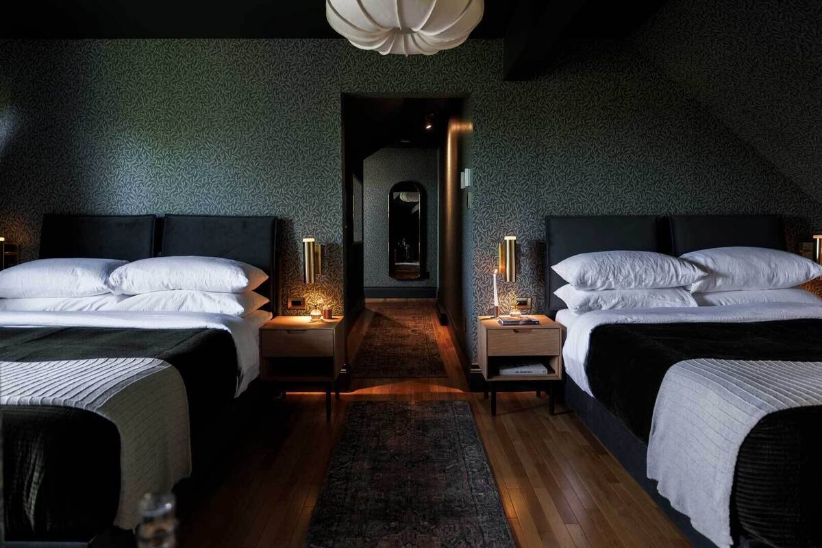 Une chambre avec deux lits, des tables de chevet avec des lampes, un mur à motifs et un plancher en bois.