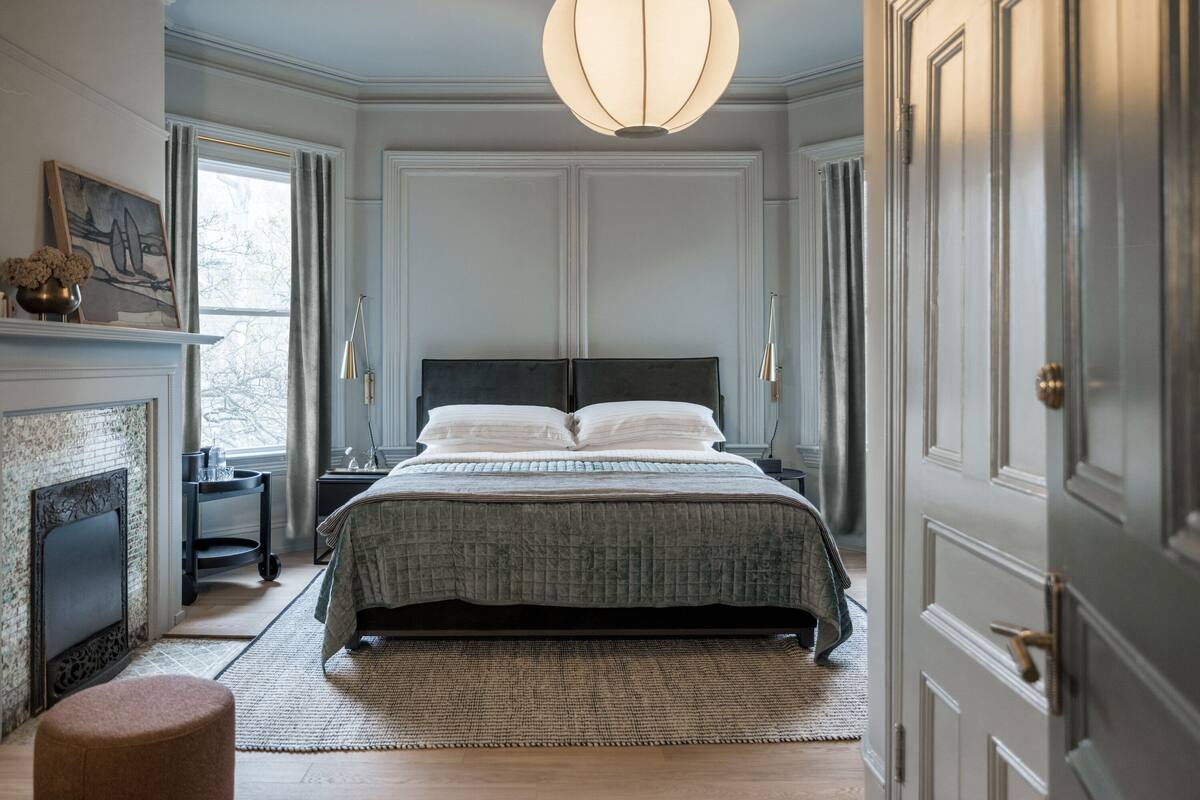 Une chambre à coucher avec un grand lit, une cheminée, un lustre et une vue par la fenêtre.