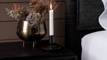 A bedside table with a metallic vase containing dried plants and a lit candle.