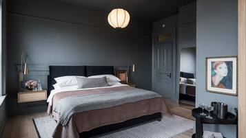 A modern bedroom with a large bed, bedside tables, a nightstand, a dresser, a painting, and a hanging light fixture.