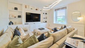 Un salón con un televisor de pantalla plana grande, muebles blancos y un ventanal con vistas.