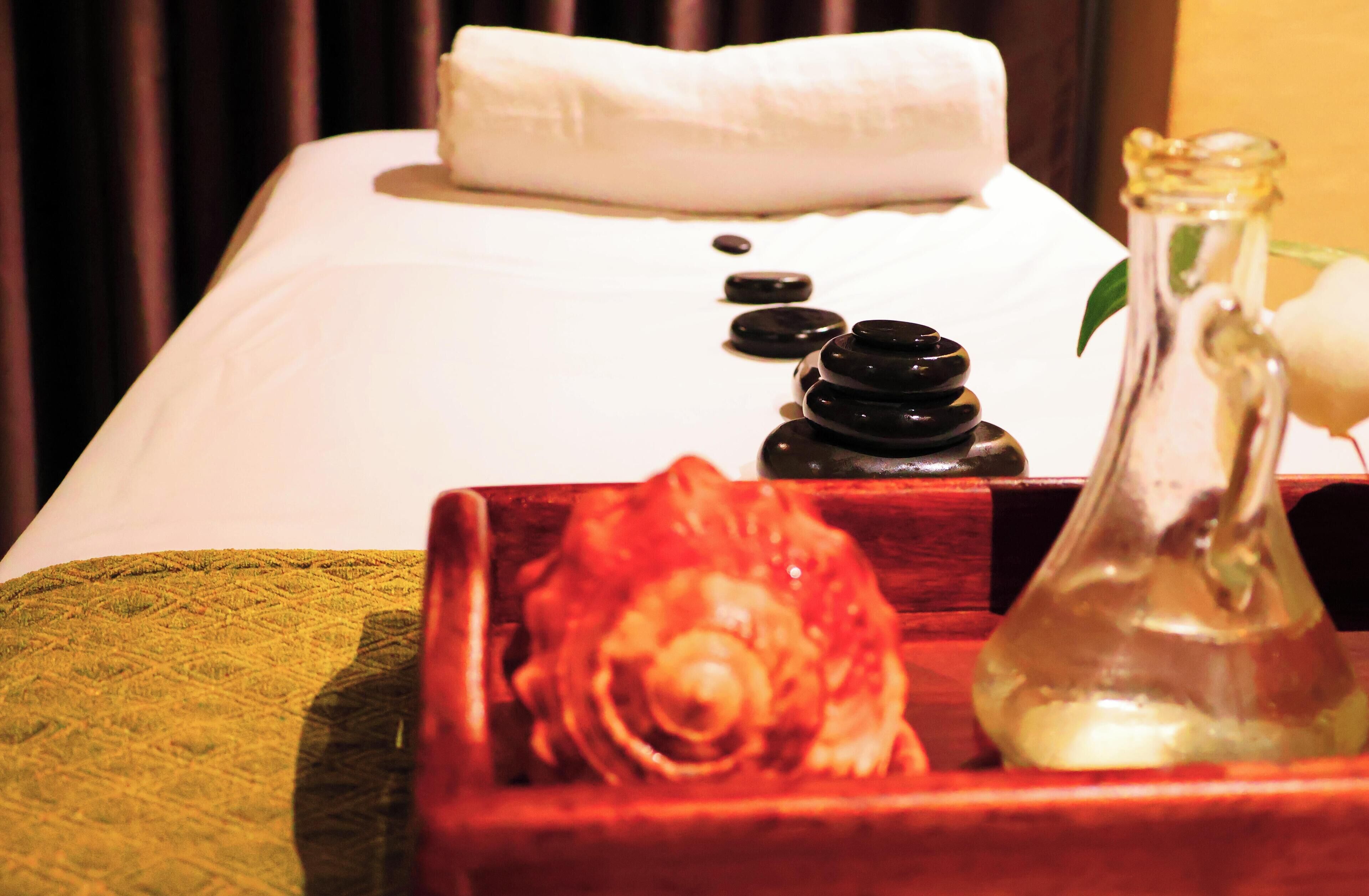 A massage table with a white towel, black stones, and a glass bottle.