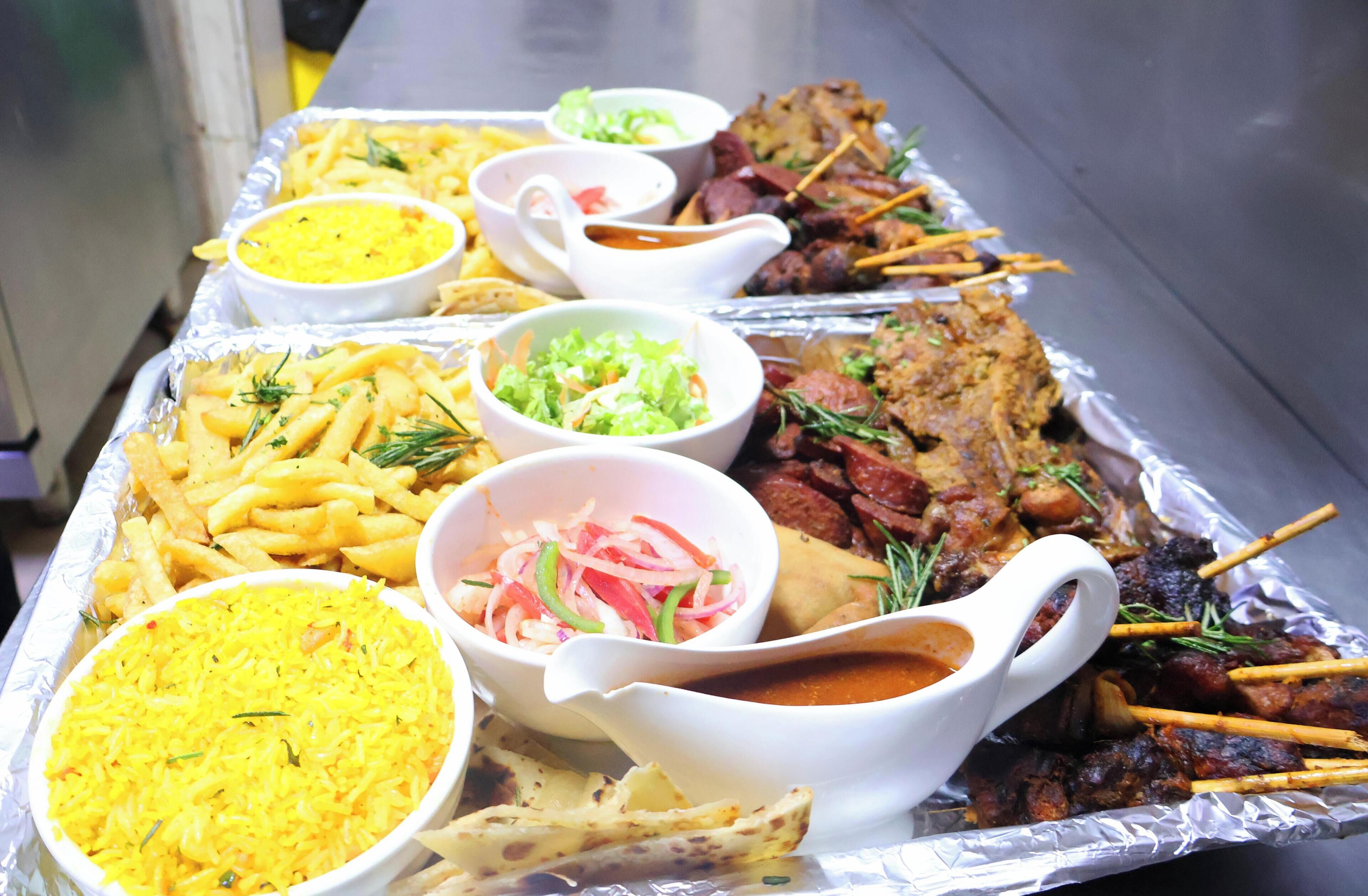 A tray of food including French fries, rice, and meat skewers, served with various condiments.