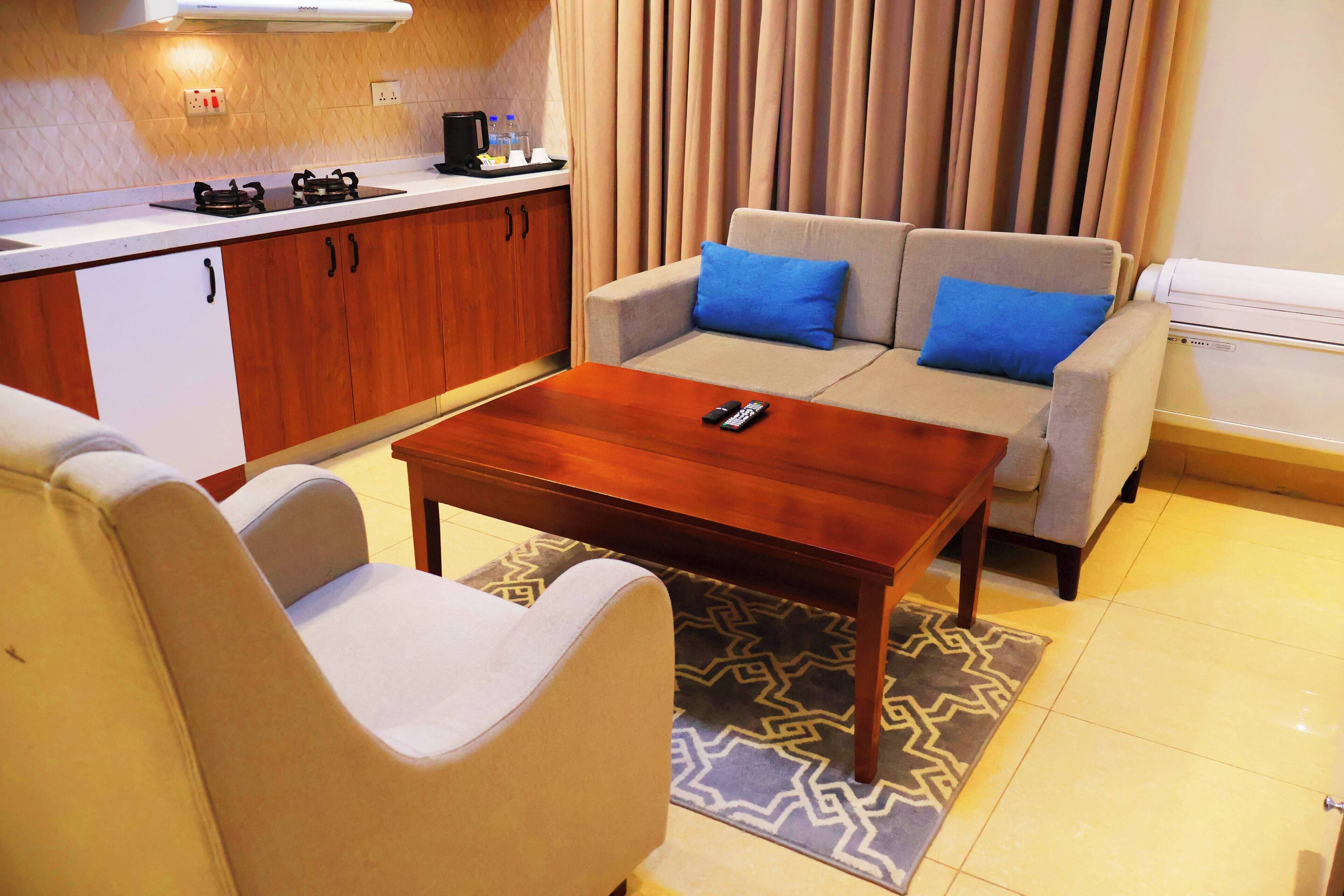 A compact living space with a kitchenette, a sofa with blue cushions, a wooden coffee table, and a patterned rug.