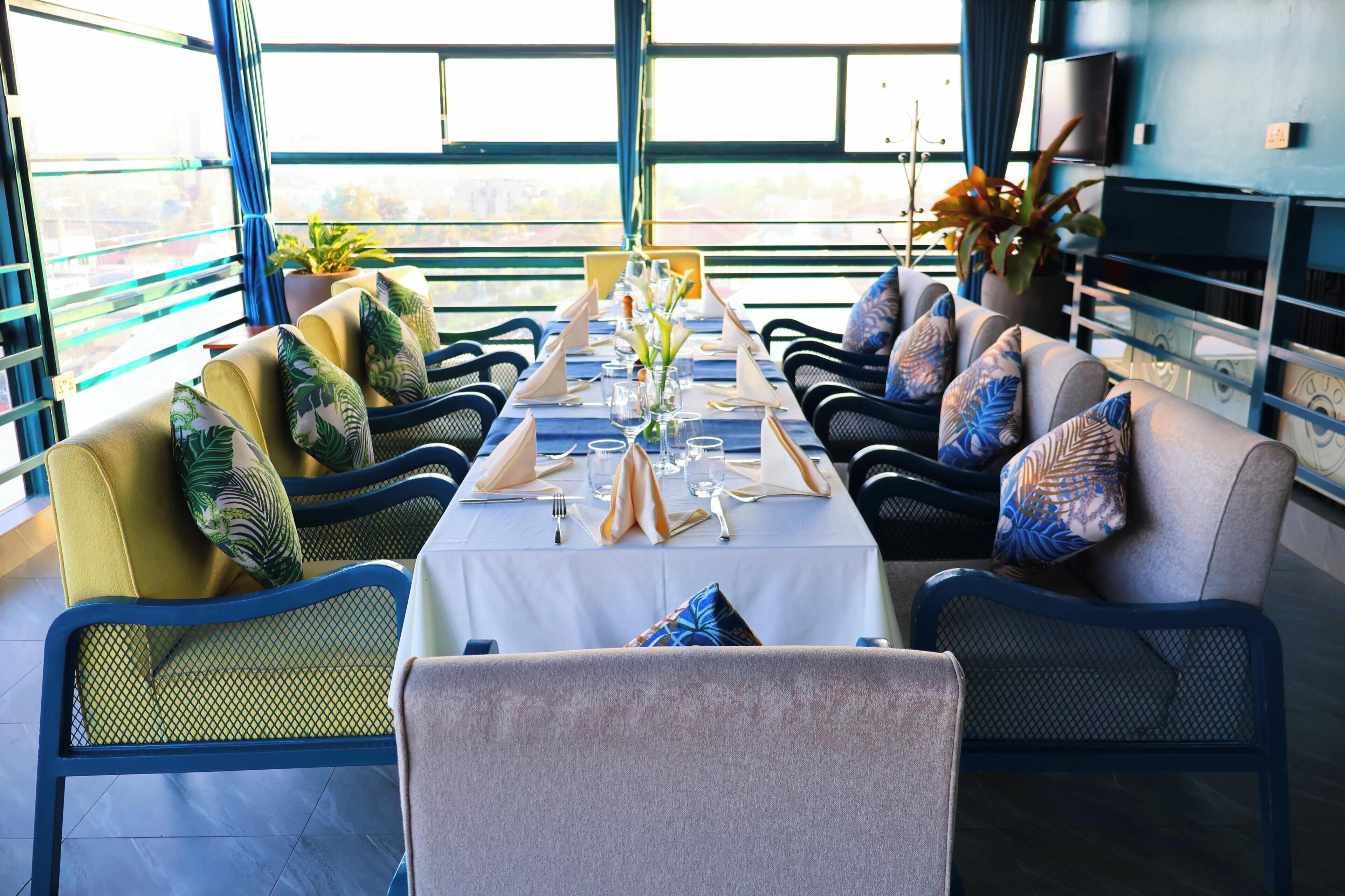 Un comedor con una mesa larga dispuesta para cuatro personas, rodeado de sillas con cojines estampados.