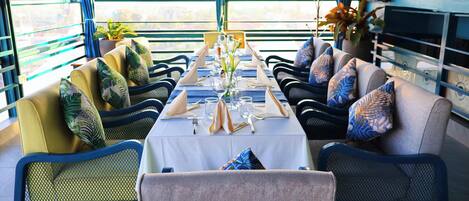 Un comedor con una mesa larga dispuesta para cuatro personas, rodeado de sillas con cojines estampados.