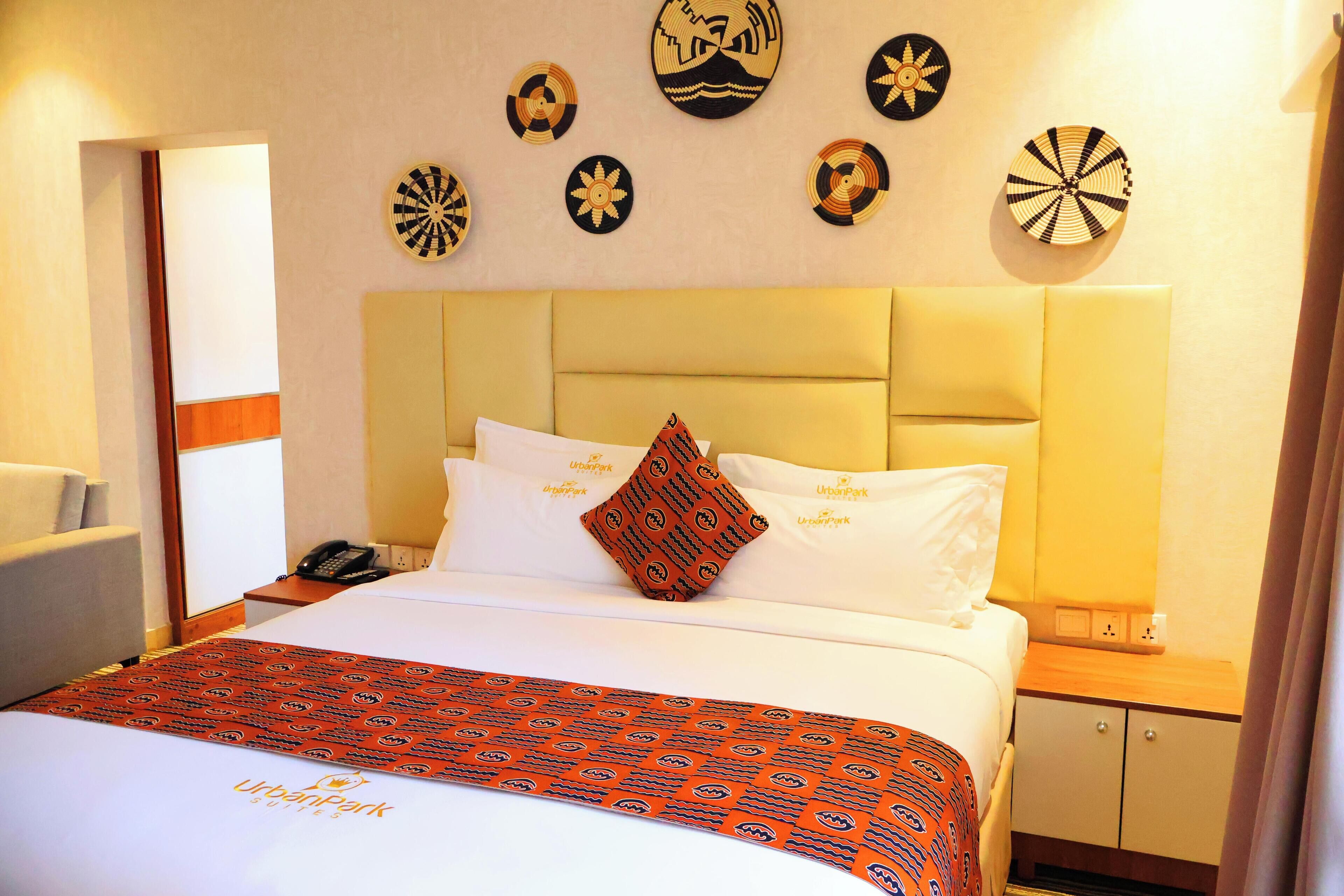 A hotel room with a bed, a bedside table with a phone, a lamp, and a wall with decorative plates.