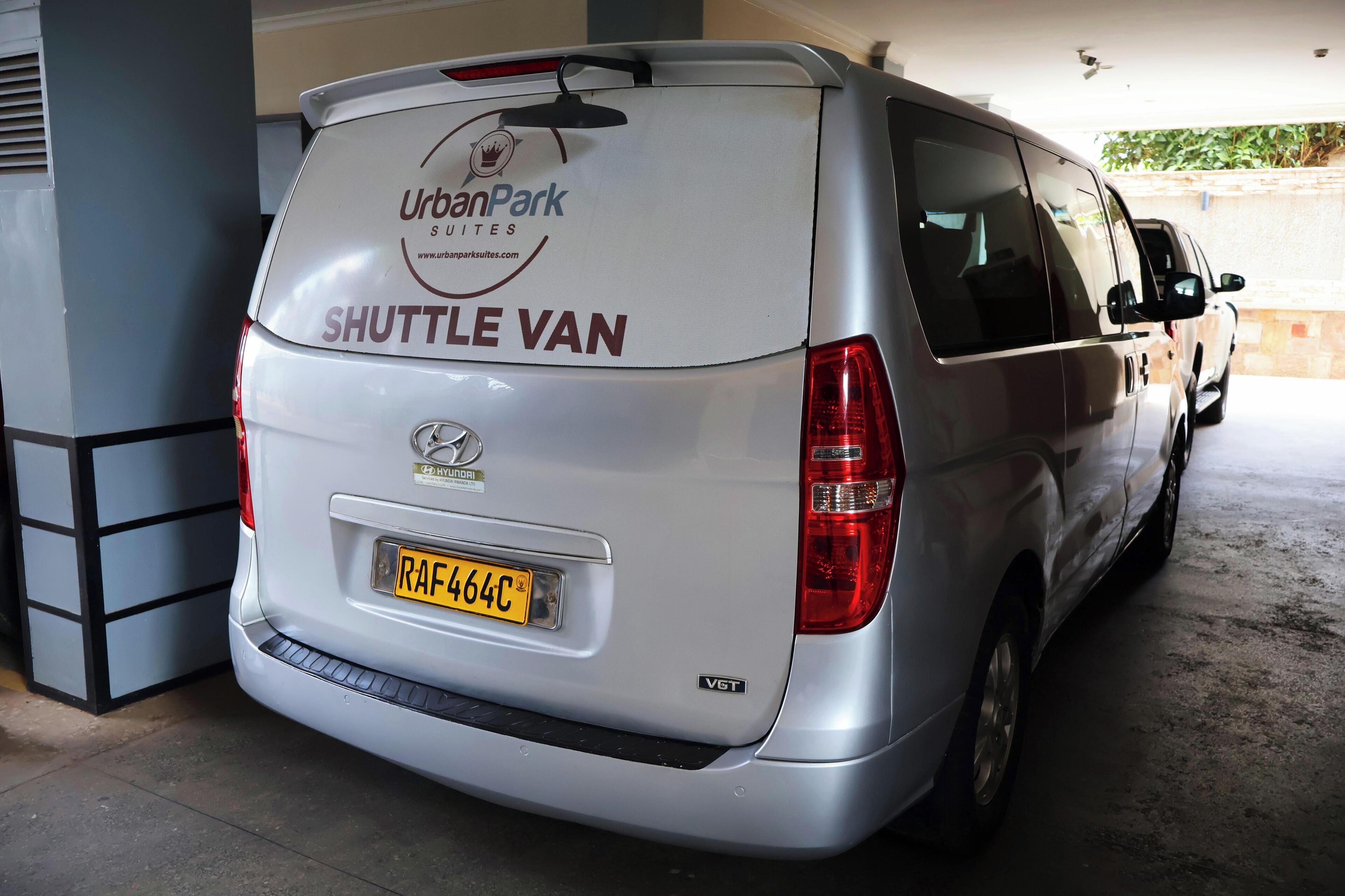 A silver shuttle van with 'UrbanPark Suites' branding and a 'SHUTTLE VAN' label.