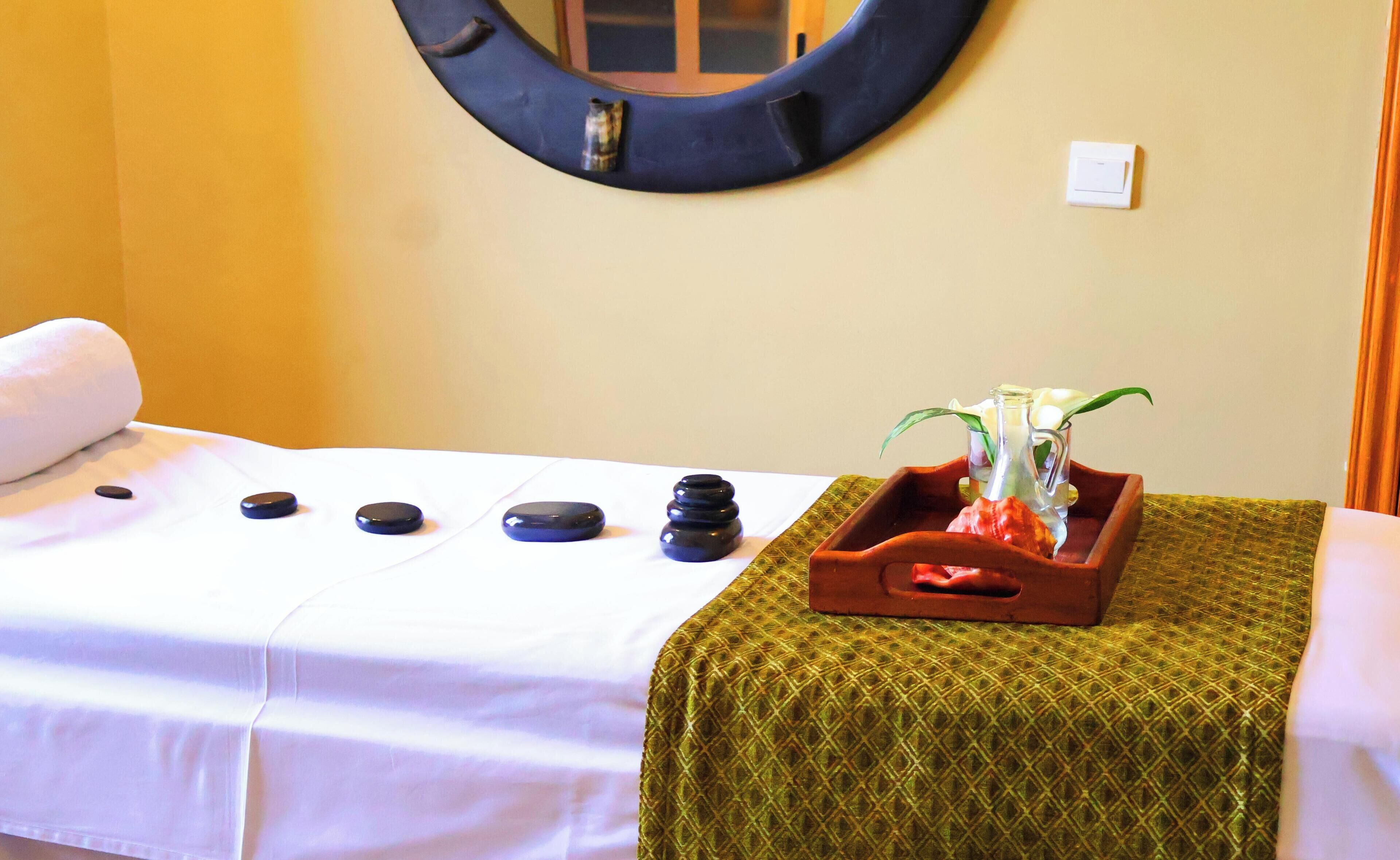 A massage table with stones, a mirror, and a tray with a plant and a bottle.