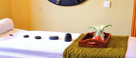 A massage table with stones, a mirror, and a tray with a plant and a bottle.