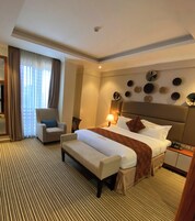 A hotel room with a large bed, a sitting area with a chair, a bedside table with a lamp, and a wall with decorative plates.