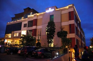 A multi-story hotel with a modern facade, illuminated signage, and a parking area with several cars.