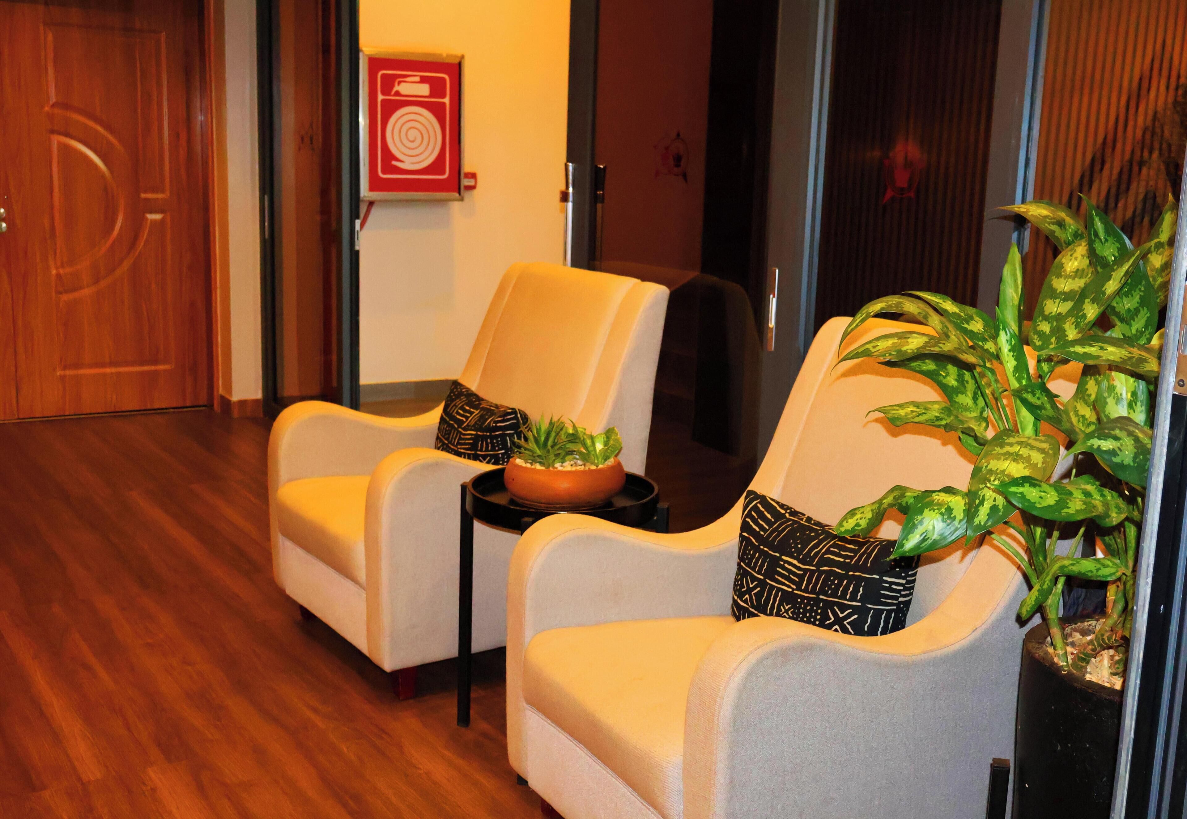 A hotel lobby with two armchairs, a small table with a plant, and a wooden floor.