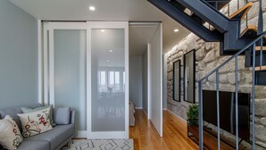 Un salon moderne avec un canapé gris, une porte-fenêtre coulissante, un escalier avec un mur en pierre et une cheminée.