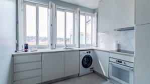 Une cuisine moderne dotée d’un lave-linge et d’un sèche-linge intégrés, de grandes fenêtres et offrant une vue sur le paysage urbain.