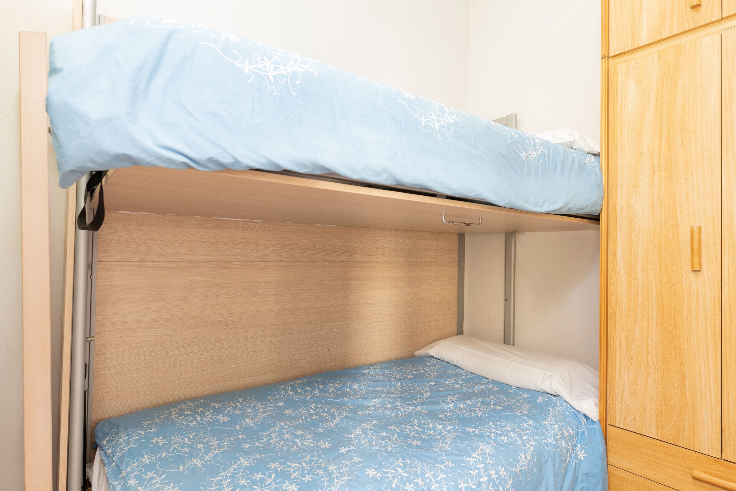Ein Etagenbett mit blumigem, blauem Bettbezug und ein Holzschrank daneben.