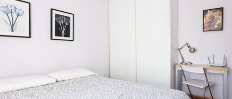 A bedroom with a bed, a desk, and a chair. There are two framed pictures on the wall.