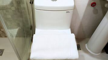 Eine weiße Toilette mit 300-mm-Messmarkierung, eine Duschkabine aus Glas und ein weißes Handtuch auf dem Sitz.